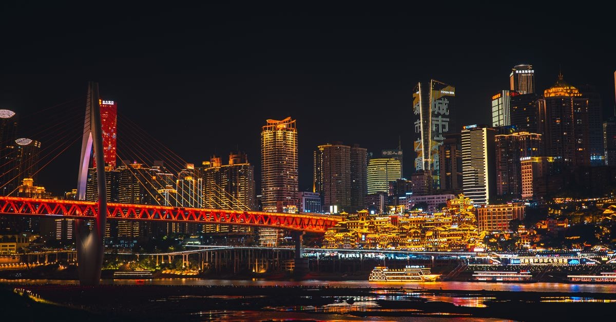 Stunning night view of Chongqing skyline with illuminated bridge over river, showcasing vibrant urban architecture.
