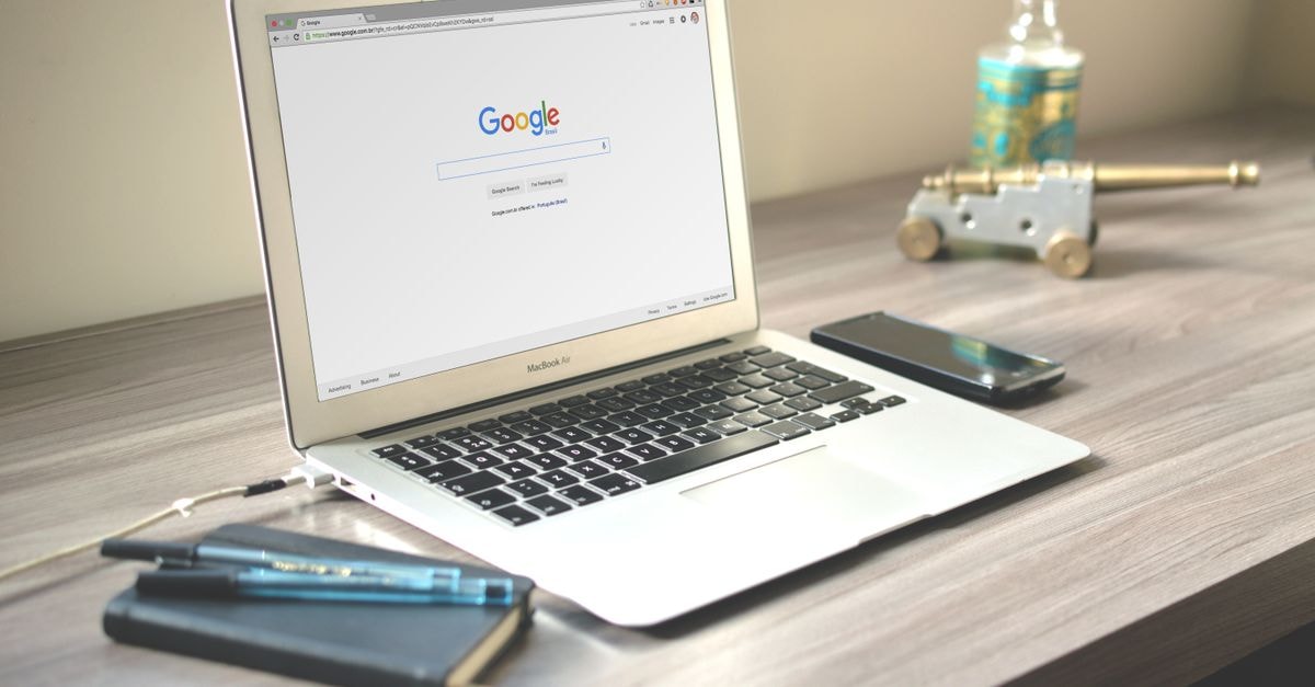 Google pulls AI image tool from Google Earth after deepfake misuse A neat workspace featuring a laptop displaying Google search, a smartphone, and a notebook on a wooden desk.