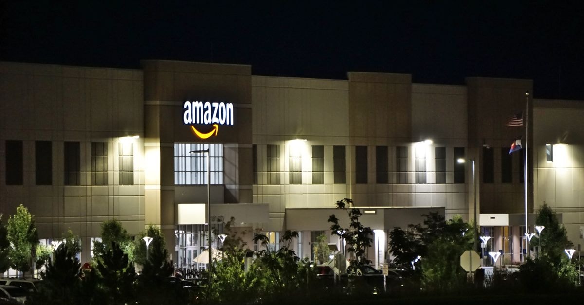 Amazon keeps 2026 capex at $220 billion as AWS growth offsets disappointing results Amazon warehouse building illuminated at night with trees and signage.
