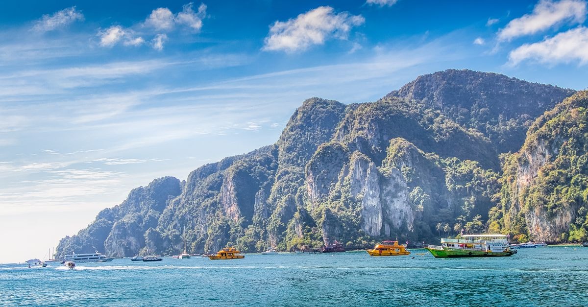 Explore the stunning limestone cliffs and serene waters of Krabi, Thailand, with colorful boats and tropical vibes.