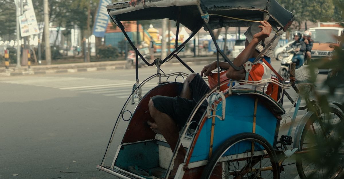 Aston Serang Hotel & Convention Center in Serang: Archipelago’s First in the City Man relaxing in a rickshaw on a busy street in Serang, Indonesia, capturing urban life.