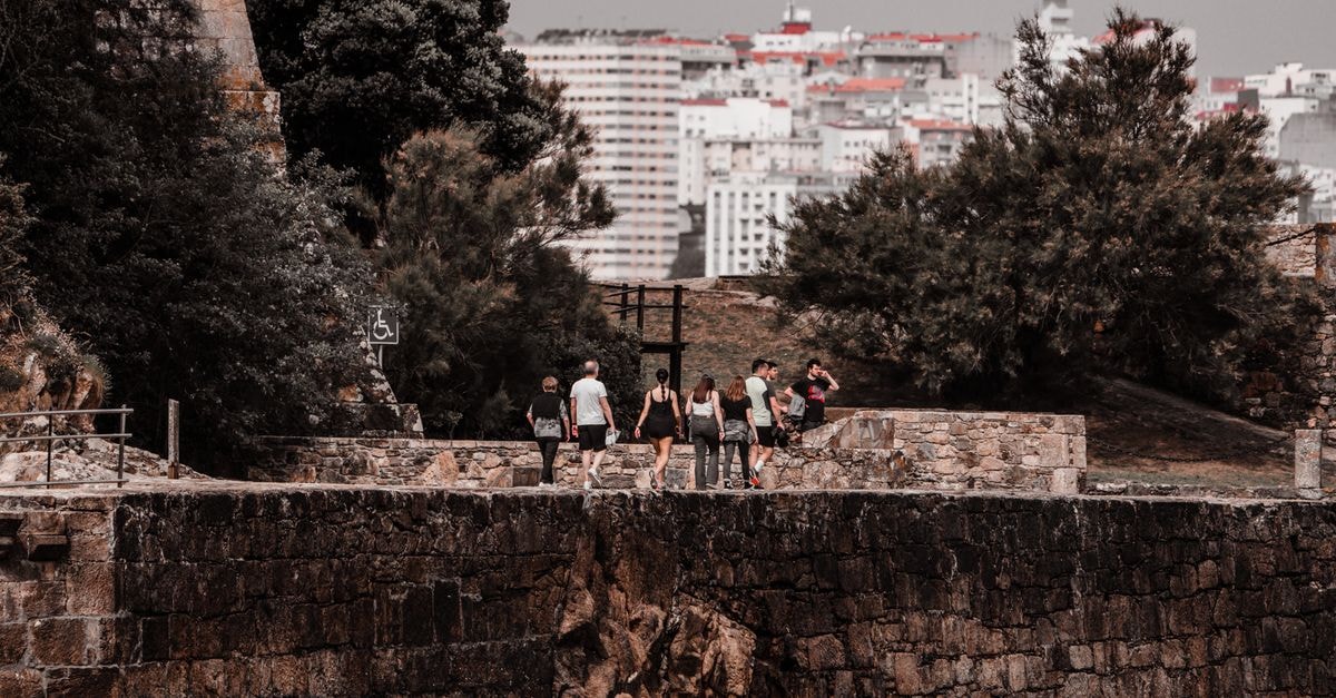 Tourists walking along the historic stone path at Porto de Santa Cruz with cityscape in background.