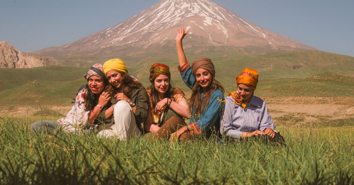 Discovering Zahedan: A Slow Travel Guide to Iran's Borderland Five women sitting in a meadow with scenic mountain backdrop, enjoying nature.