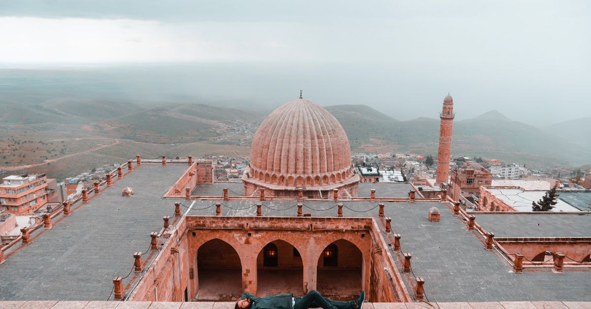 Aerial perspective of a historic mosque with a person relaxing on the rooftop.