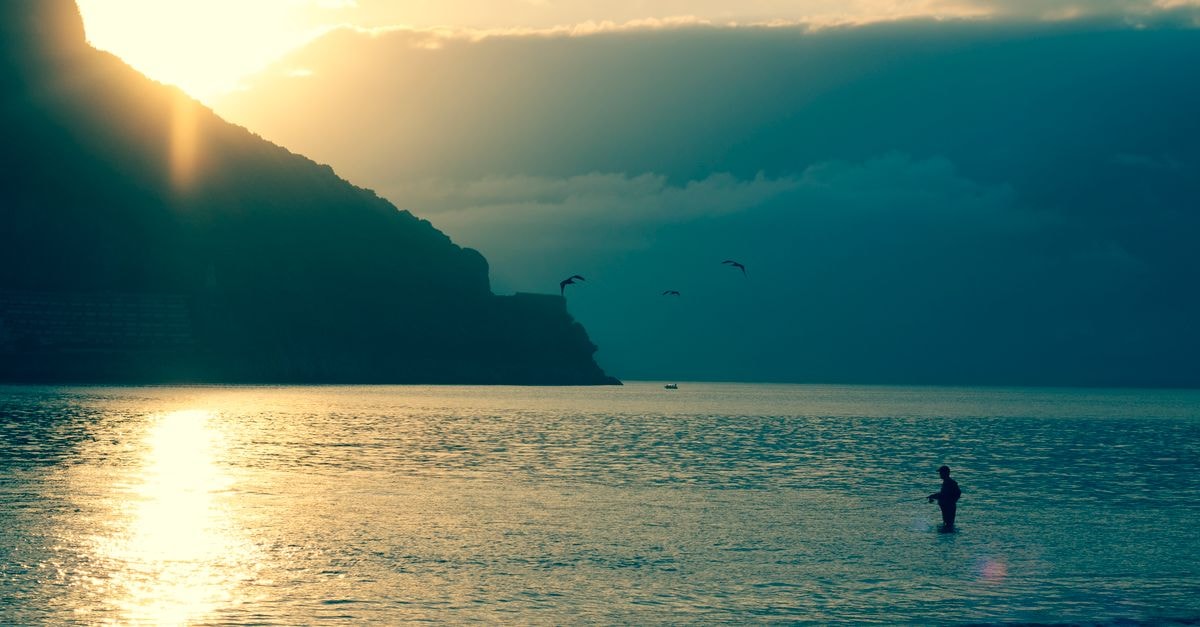 拉雷多海灘的寧靜景緻，夕陽背景下漁夫與鳥群的剪影。