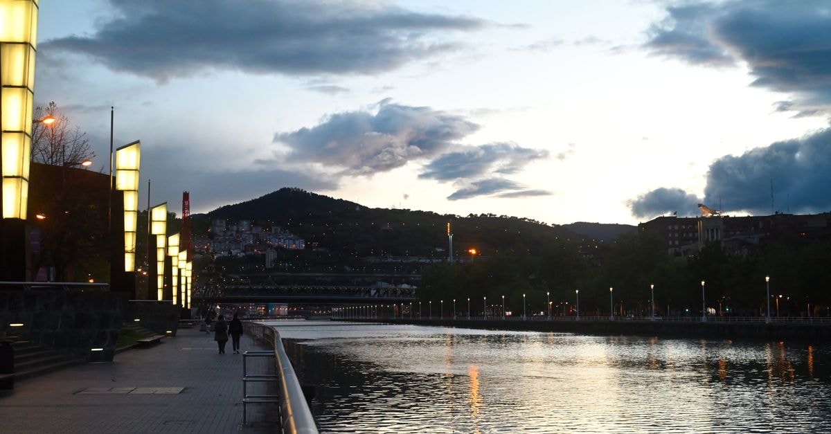 Sercotel Coliseo Bilbao: A Stay Inside a Former Opera Venue Evening view of the illuminated riverfront in Bilbao, Spain, showcasing vibrant city lights and a serene water reflection.