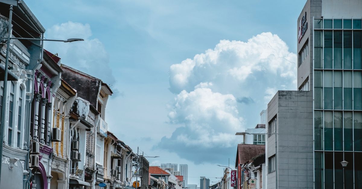 Johor Bahru Travel Guide: A Slow Look at Malaysia's Southernmost City A bustling city street lined with colonial-era buildings and a modern office under a cloud-filled sky.