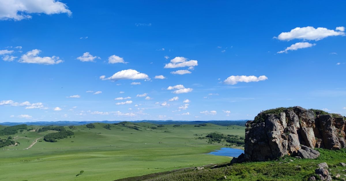 Dingxi Travel Guide: Potatoes, Plateaus, and a Quiet Northwest Stop A breathtaking view of expansive grasslands under a bright blue sky, featuring a rugged rocky outcrop.