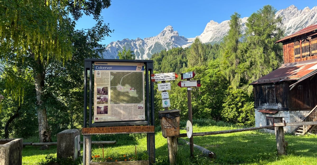 Information board and signs in a mountain village with scenic alpine background.