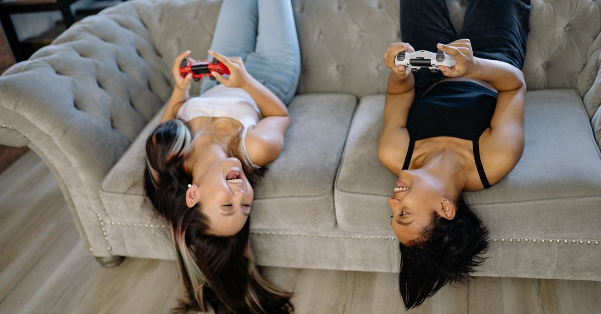 Game Your Game rolls out GameGolf KZN AI to all golfers Two women having fun playing video games upside down on a sofa indoors.