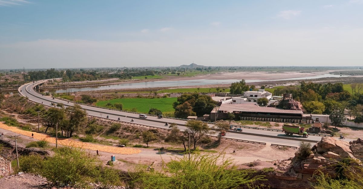 Meerut Travel Guide: Weather, Getting Around, and What to Eat Wide-angle view of highway curving through scenic landscape with river and lush fields under a clear blue sky.