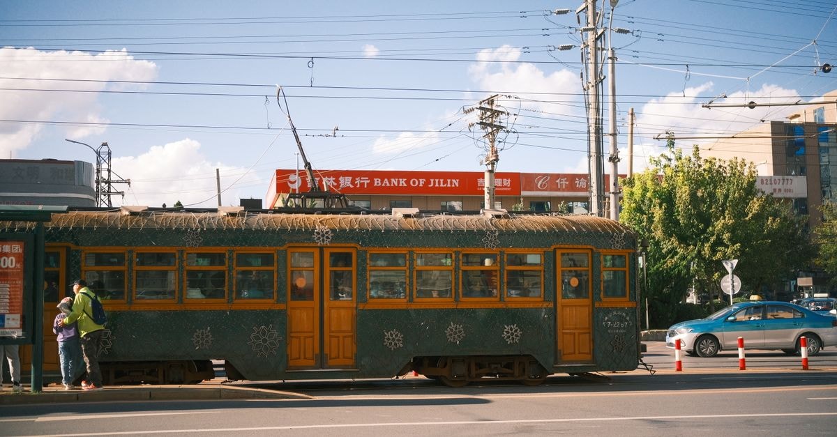 Vintage tram travels through city street near Bank of Jilin under clear skies.