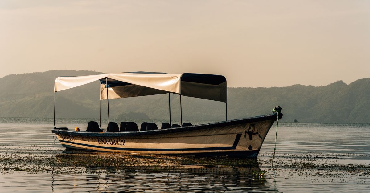 Zumpango Travel Guide: Lakeside History and Local Flavor A tranquil boat on a calm lake with volcanic hills in the backdrop in El Salvador at dawn.