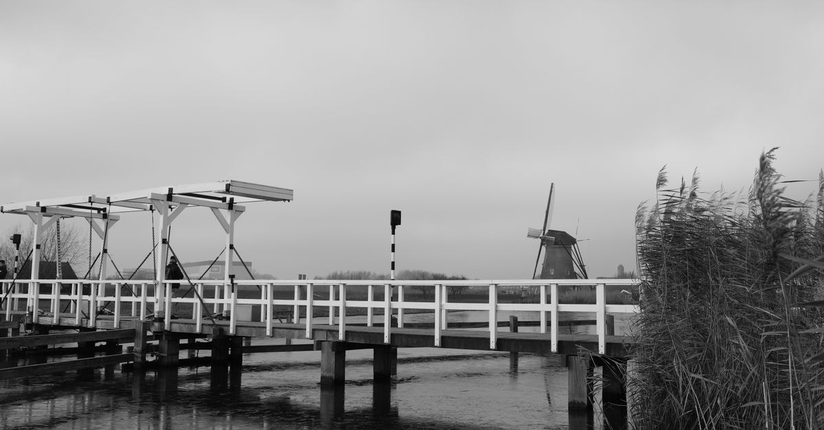 Scenic black and white photo of the iconic Kinderdijk windmill and bridge, Holland.