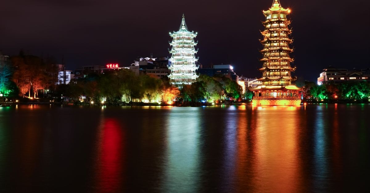 Hotel Universal Guilin in Guilin — A Li River Address Near Jiefang Bridge A stunning night view of the illuminated Sun and Moon Pagodas reflecting in a serene river in Guilin, China.