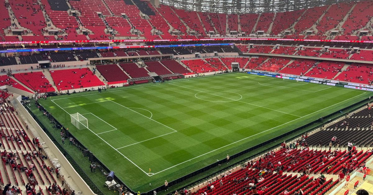 A comprehensive aerial view of a modern stadium with red seats and green field.