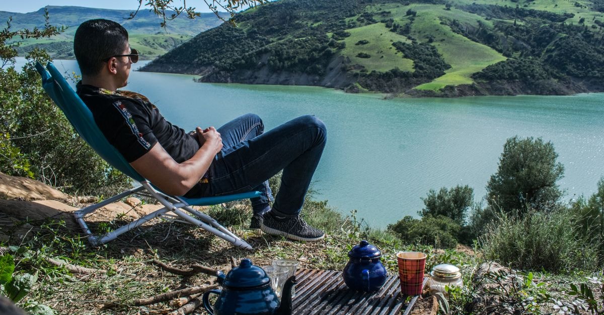 A man relaxing by a scenic lake in Blida, Algeria, surrounded by hills and greenery.