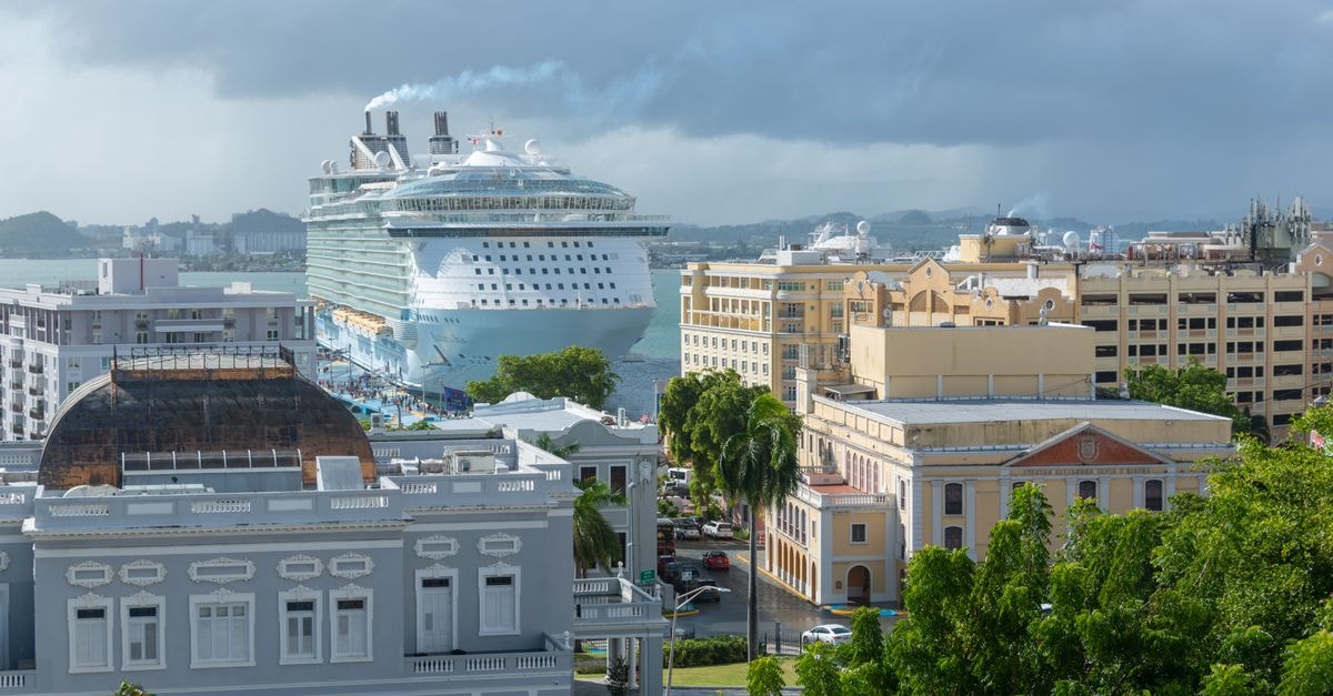 A large cruise ship moored in a vibrant urban harbor, surrounded by historic architecture.