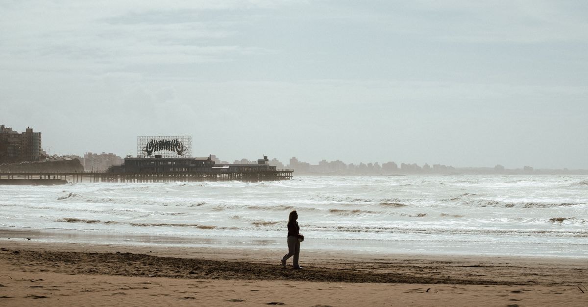 Viña del Mar travel guide: coastal calm meets Chilean port energy A lone person walks along a deserted beach with a vintage pier in the background.