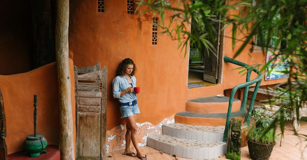 Matagalpa Travel Guide: Into Nicaragua's Coffee Highlands Full body brunette wearing denim clothes with cup of hot drink leaning on rural cottage wall while visiting exotic tropical country