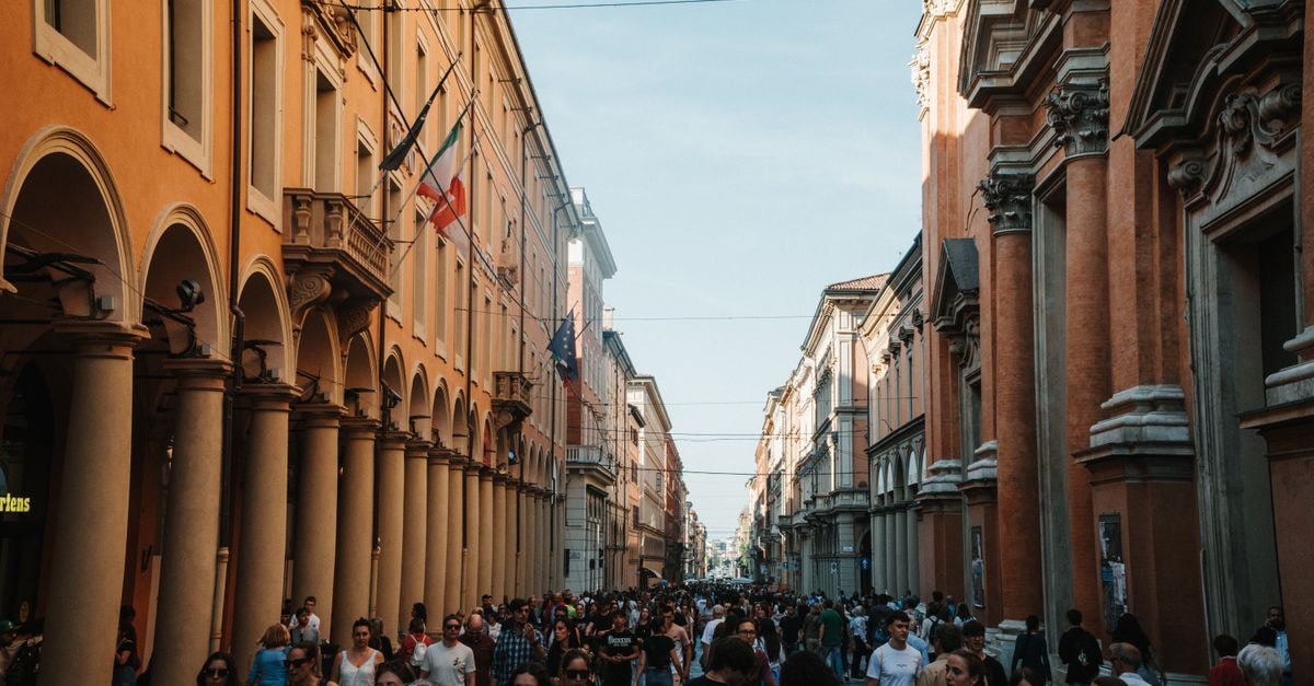 Buonhotel Bologna in Bologna: A Restored 1200s Stay Near Piazza Maggiore A vibrant urban scene in Bologna, Italy, showcasing historic architecture and a lively crowd.