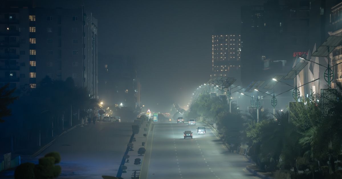 Atmospheric night street in Karachi, Pakistan enveloped in fog and city lights, creating a moody urban scene.