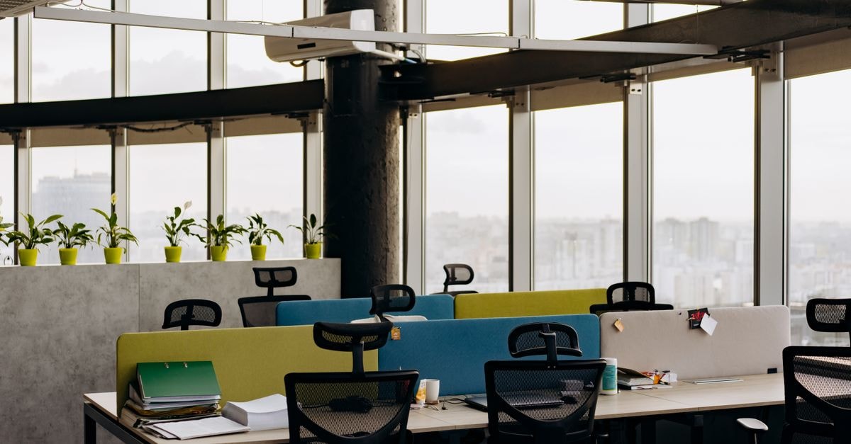 A spacious open office with colorful dividers, large windows, and a cityscape view, perfect for creative work environments.