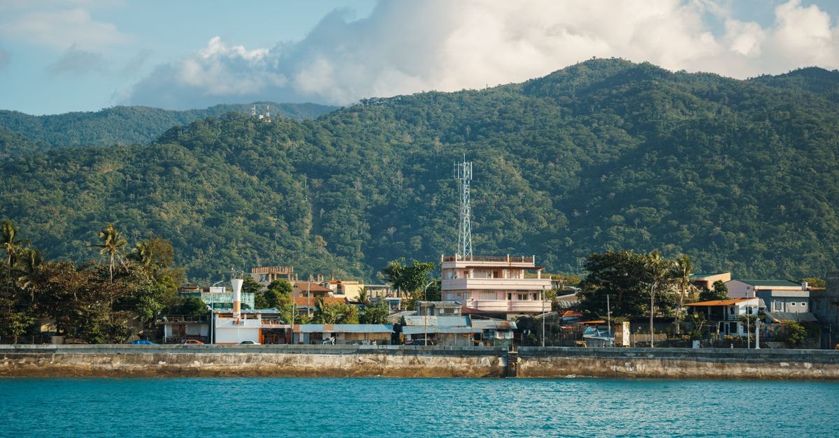 A picturesque coastal village with lush mountains in the background on a sunny day.