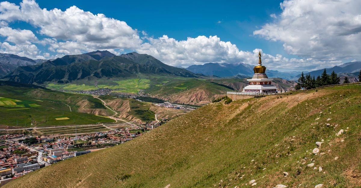 Bazhong Travel Guide: Planning Tips, Costs and Things to Do Scenic summer view of a Tibetan landscape featuring mountains, a small town, and a hilltop monastery.