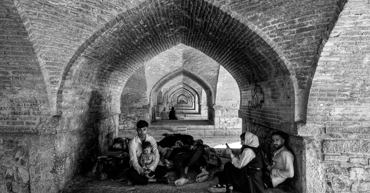 Keryas Hotel in Isfahan: A Qajar-Era Mansion Reimagined Black and white photo of people resting under the arches of a historic bridge in Esfahan, Iran.