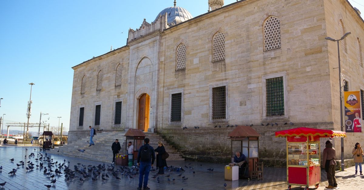 Scene of people and pigeons in front of a historical mosque on a sunny day.