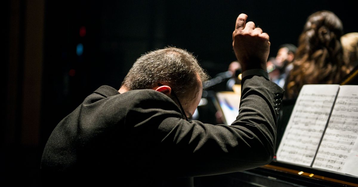 A conductor passionately leads an orchestra during a live performance with visible sheet music.