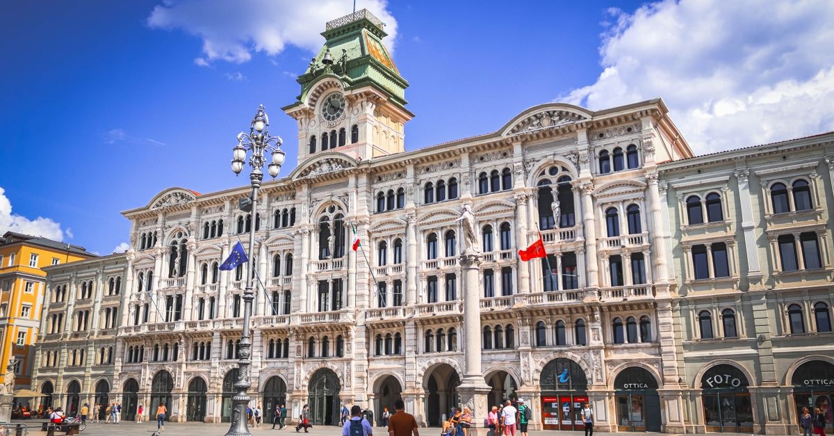 DoubleTree by Hilton Trieste in Trieste: a 1900s palace reborn near Piazza Unità Daytime shot of Trieste City Hall's elegant architecture in Italy with people and flags displayed.