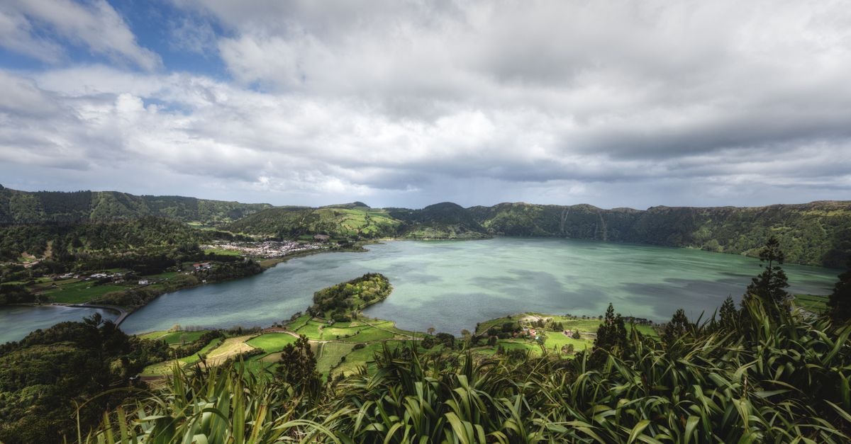 A stunning view of the Lagoa das Sete Cidades, surrounded by lush greenery under a cloudy sky.
