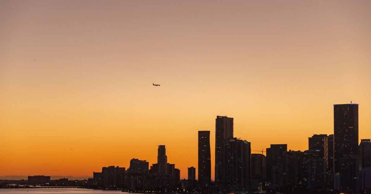 JW Marriott Marquis Miami: Arts, Culture, and the Downtown Bayfront Stunning city skyline during sunset with an airplane flying above, creating a serene urban landscape.