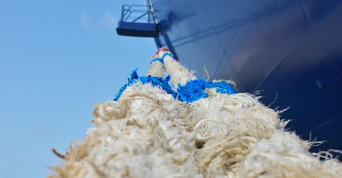 Detailed close-up of a heavy rope mooring line attached to a ship's hull with a clear blue sky background.