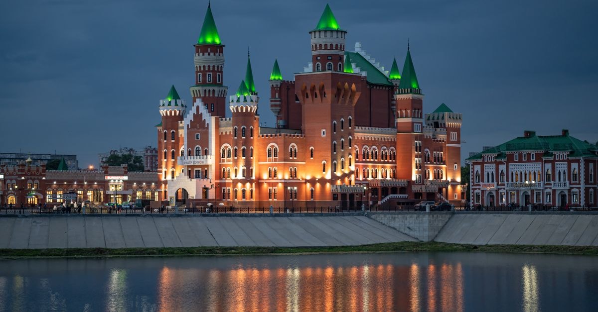 A picturesque view of a brightly lit castle with reflection in the river under the night sky.