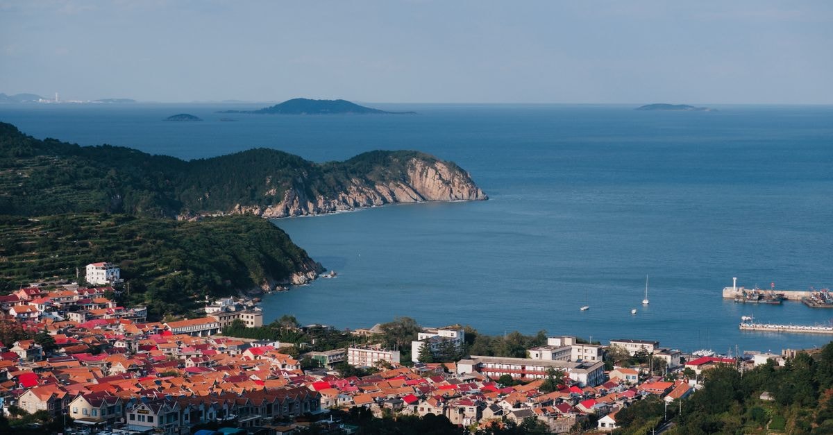 Ningde Travel Guide: Coast, Mountains, and She Culture Aerial view of a picturesque coastal town with red-roofed houses, lush greenery, and calm blue ocean.