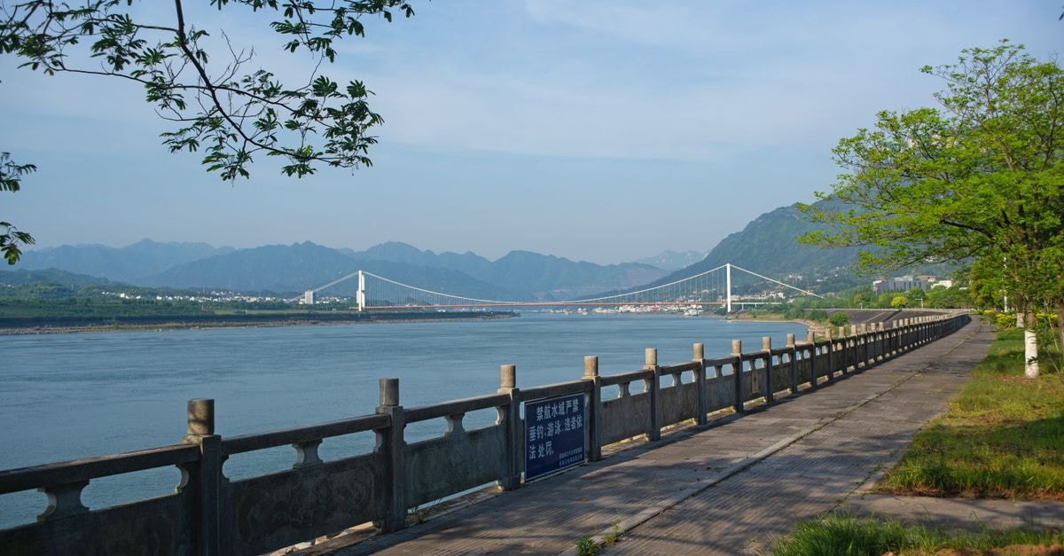 Wyndham Grand Yichang Riverside — Sky-High Luxury on the Yangtze A picturesque view of a bridge spanning the Yangtze River under a blue sky with mountains.