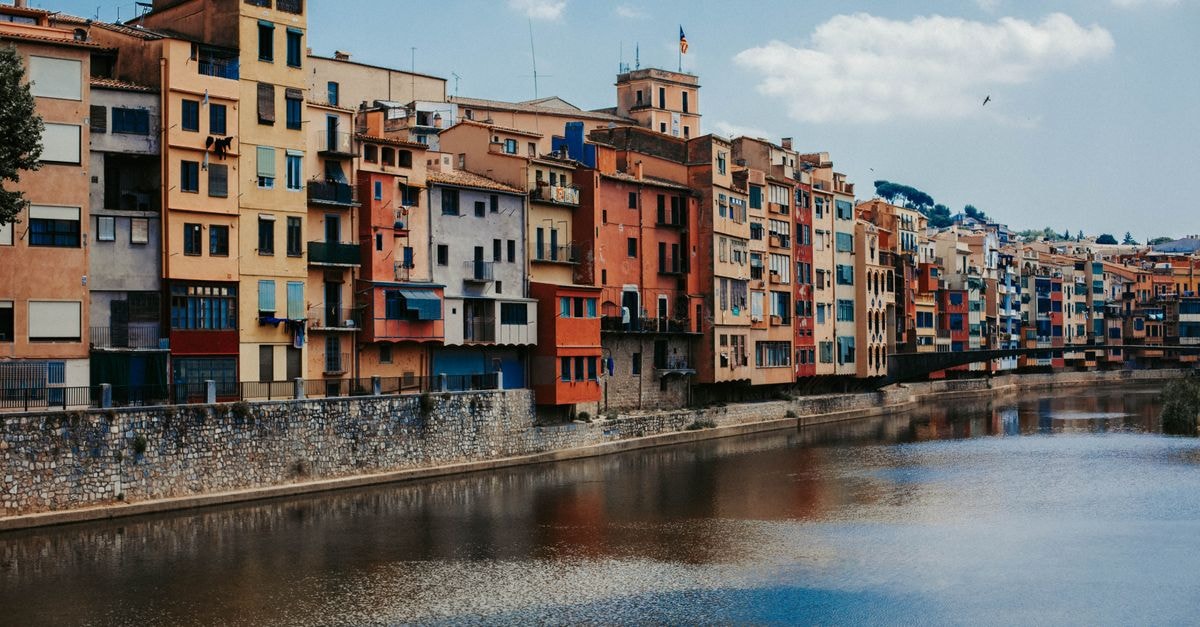 Vibrant apartment facades line the Onyar River in Girona, Spain, reflecting architectural beauty.