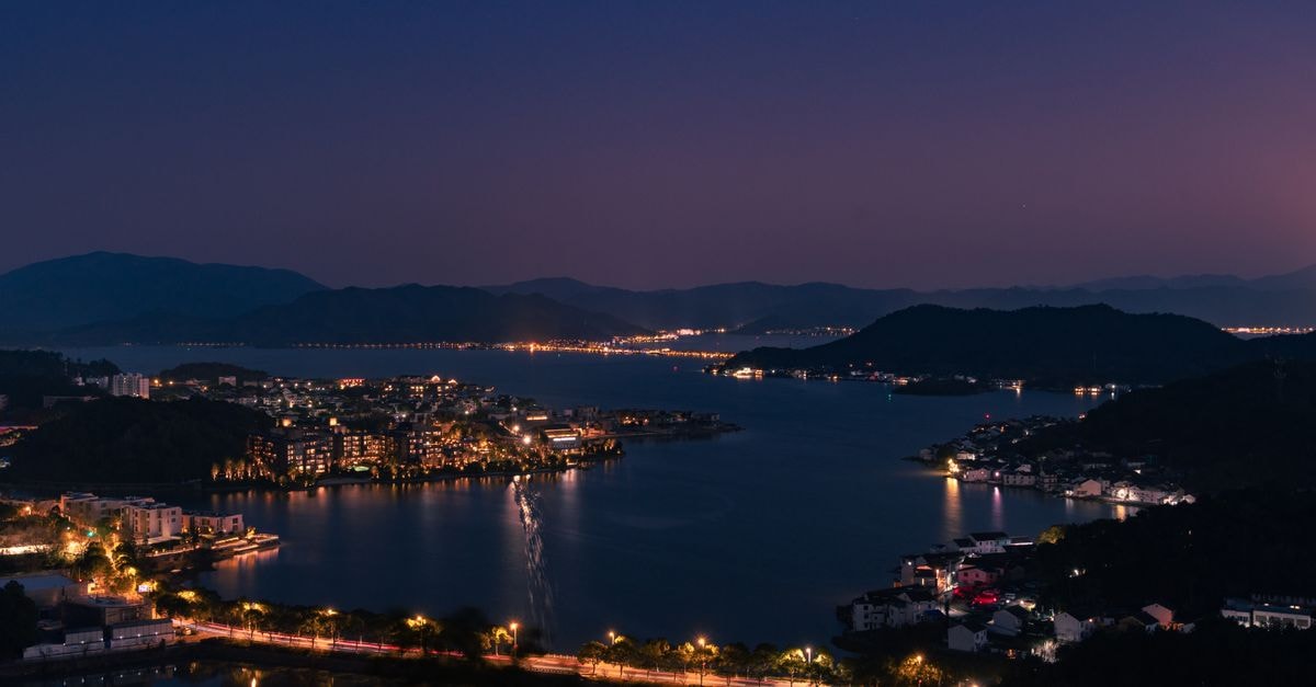 Liuzhou Travel Guide: Planning Tips, Costs and Things to Do Serene twilight view of a city skyline reflecting over a calm lake, surrounded by mountains.