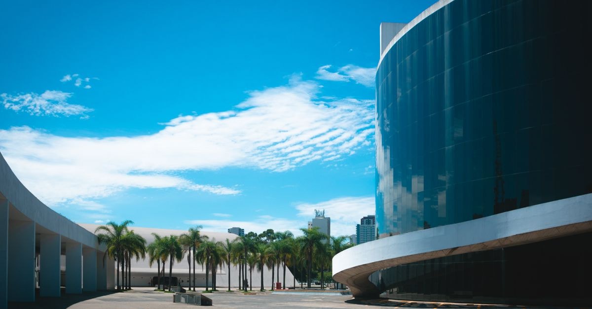 Goiânia Palace Hotel in Goiânia: Art Deco Stay Near Praça Dr. Pedro Ludovico Modern glass building showcasing urban architecture amidst palm trees and blue skies.
