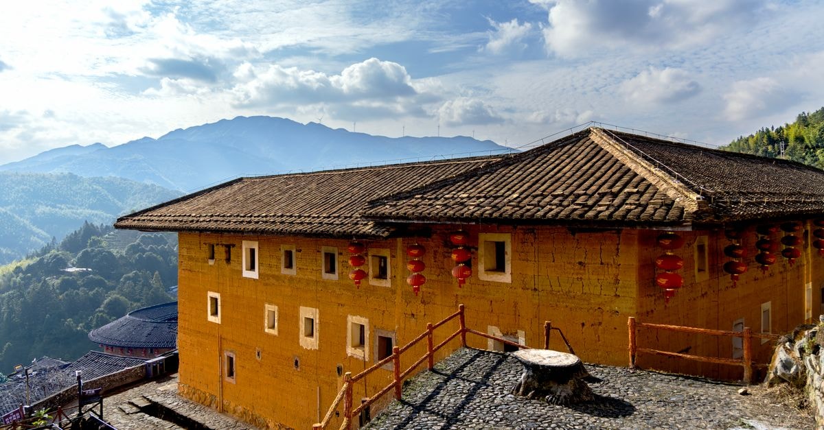 Xiangyang Travel Guide: Planning Tips, Costs and Things to Do Scenic view of a traditional Fujian Tulou with mountains in the background under clear skies.
