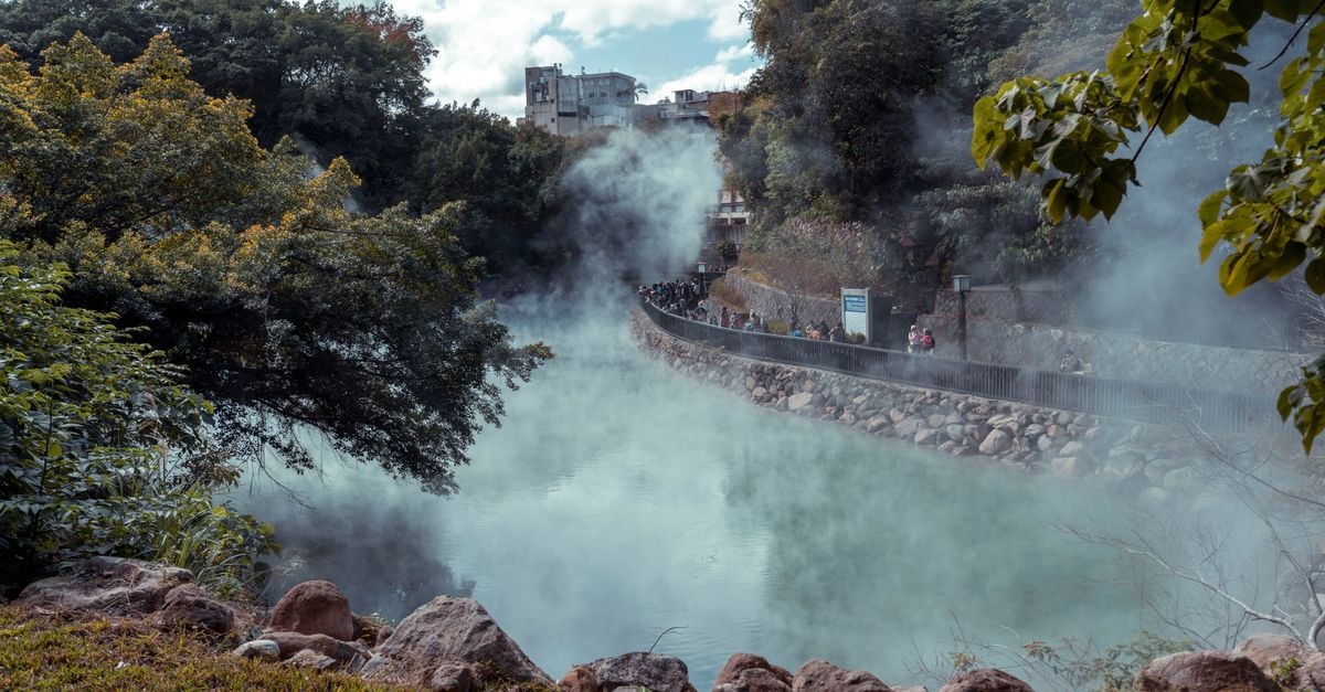 Ankang Travel Guide: River Lakes, Hot Springs, and Shaanxi Noodles A serene hot spring landscape with steam rising amidst lush greenery, attracting tourists.