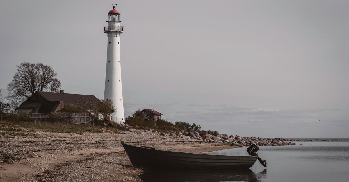 Peaceful coastal scene with a lighthouse, boat, and calm sea on Kihnu Island, Estonia.