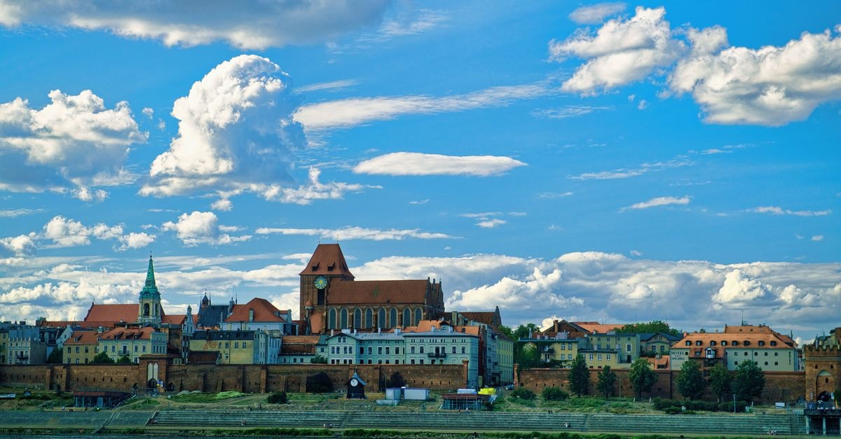 Torun Travel Guide: Planning Tips, Costs and Things to Do Beautiful view of Torun's old town by the river under a vibrant blue sky.