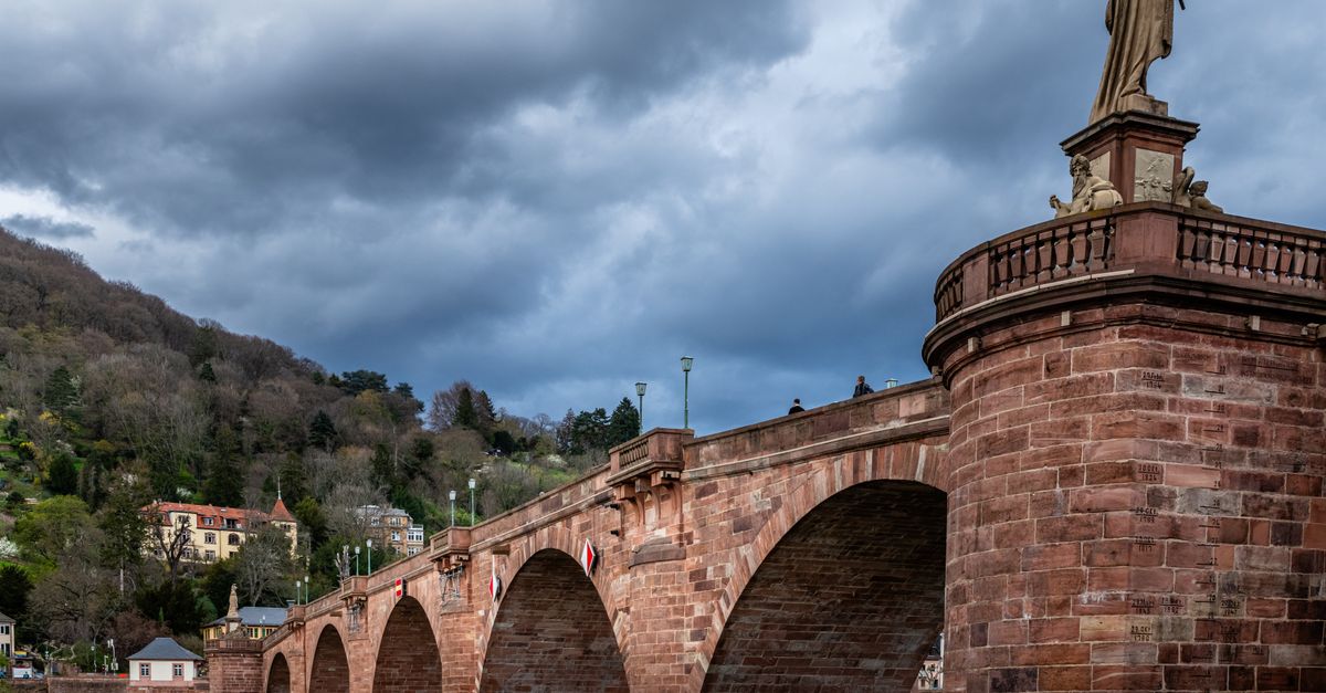 Historic Heidelberg's Old Bridge spanning the Neckar River against dramatic clouds.