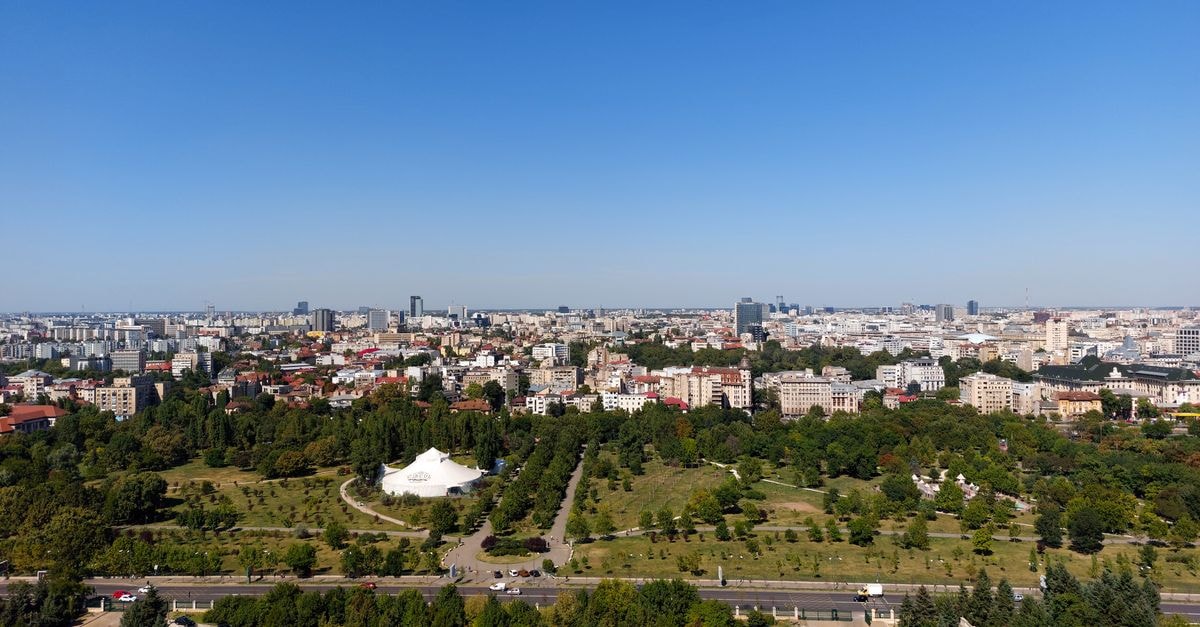 Hotel Ramada in Pitești: Business Meets Relaxation Aerial view of Bucharest cityscape with green parks and skyline under clear blue sky.