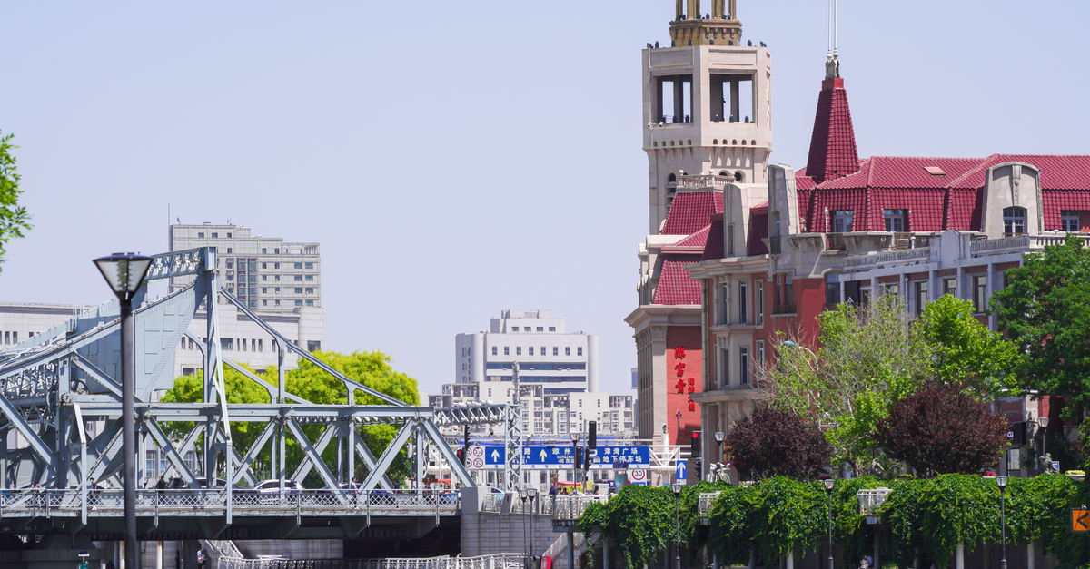 Tanggu travel guide: finding the port rhythm of Tianjin A vibrant cityscape of Tianjin featuring a historic bell tower, steel bridge, and lush greenery.