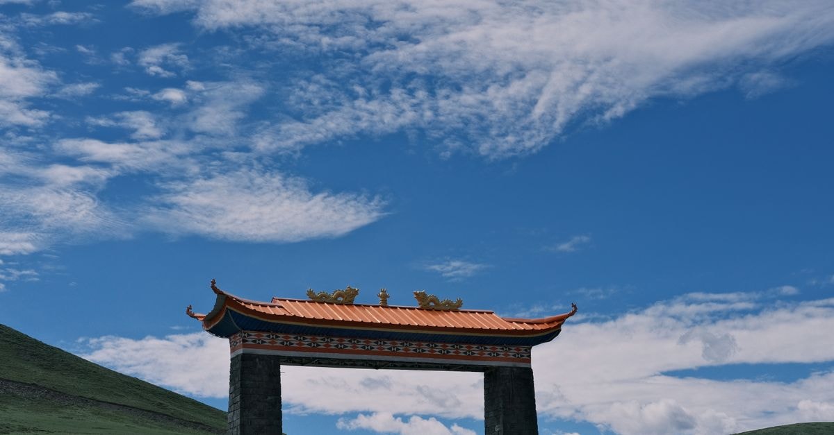 Yining Travel Guide: Gateway to Xinjiang's Ili Valley A decorative traditional gate against a backdrop of lush hills and blue sky, capturing serene beauty.
